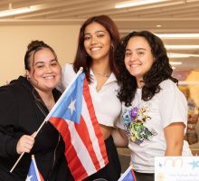 Three students stand together for a photo. One furthest on the left is holding a Puerto Rican flag.