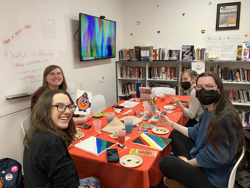 Four students sitting together at a table and painting.