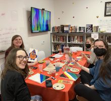 Four students sitting together at a table and painting.
