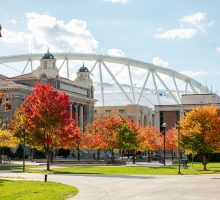 Autumn trees with vibrant colors on the quad with Carnegie Library and the stadium in the background.