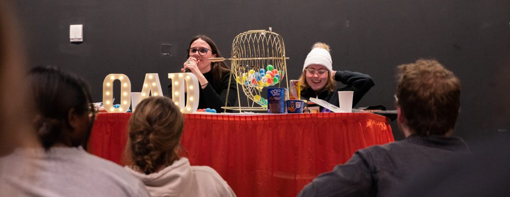 Two students sit at table with bingo ball spinner