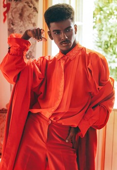 A person wearing a red monochrome looks with an overcoat, puffed button up and highwaisted slacks.