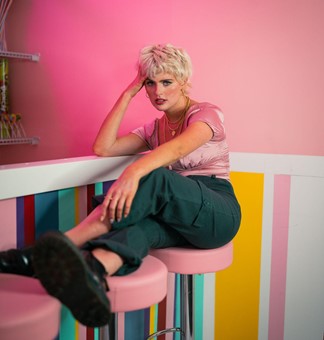 A person wearing jewel tones and posing on stool.