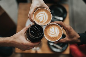 Three people holding hot lattes, “cheersing” their cups.