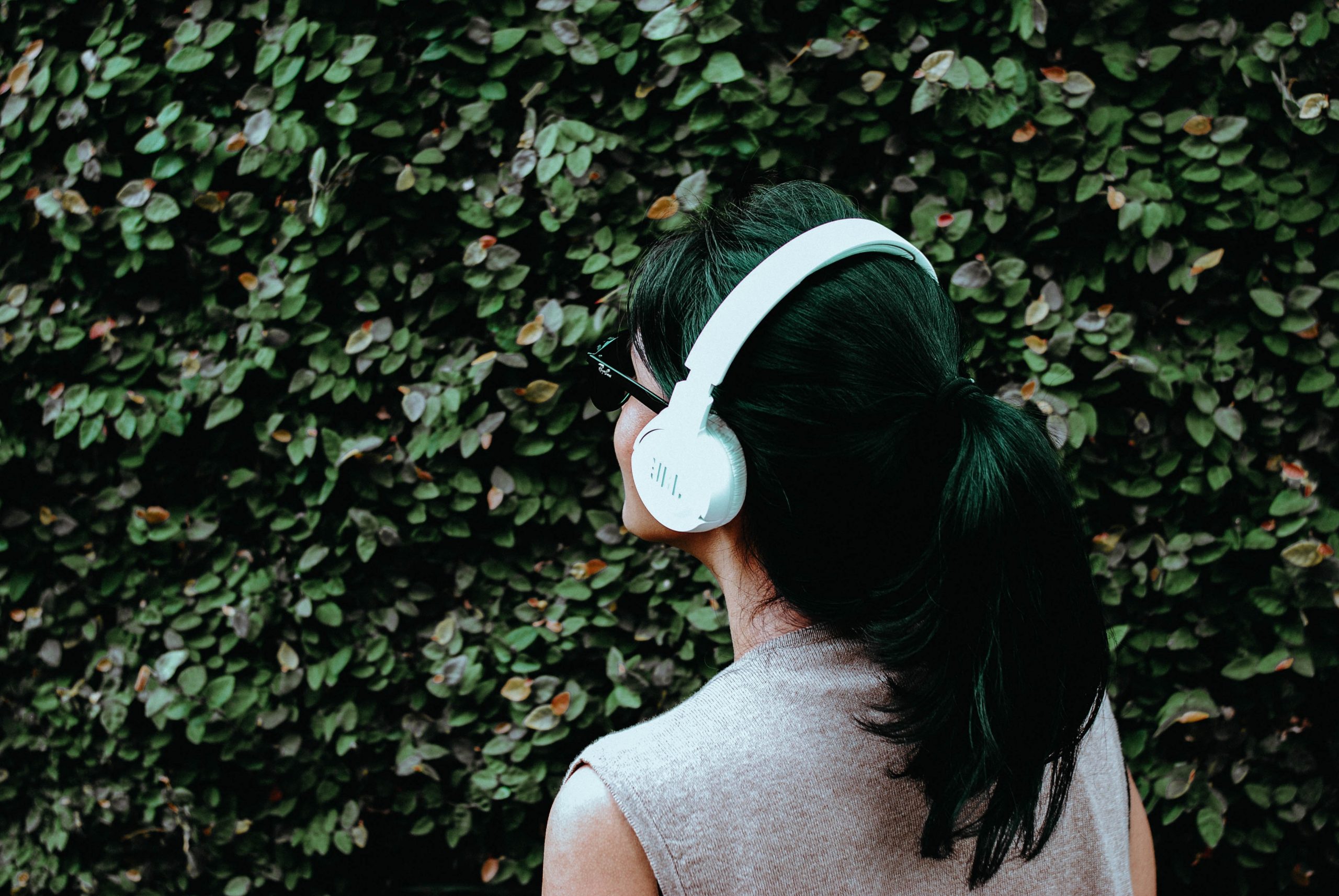 Person wearing white headphones with back turned to camera.