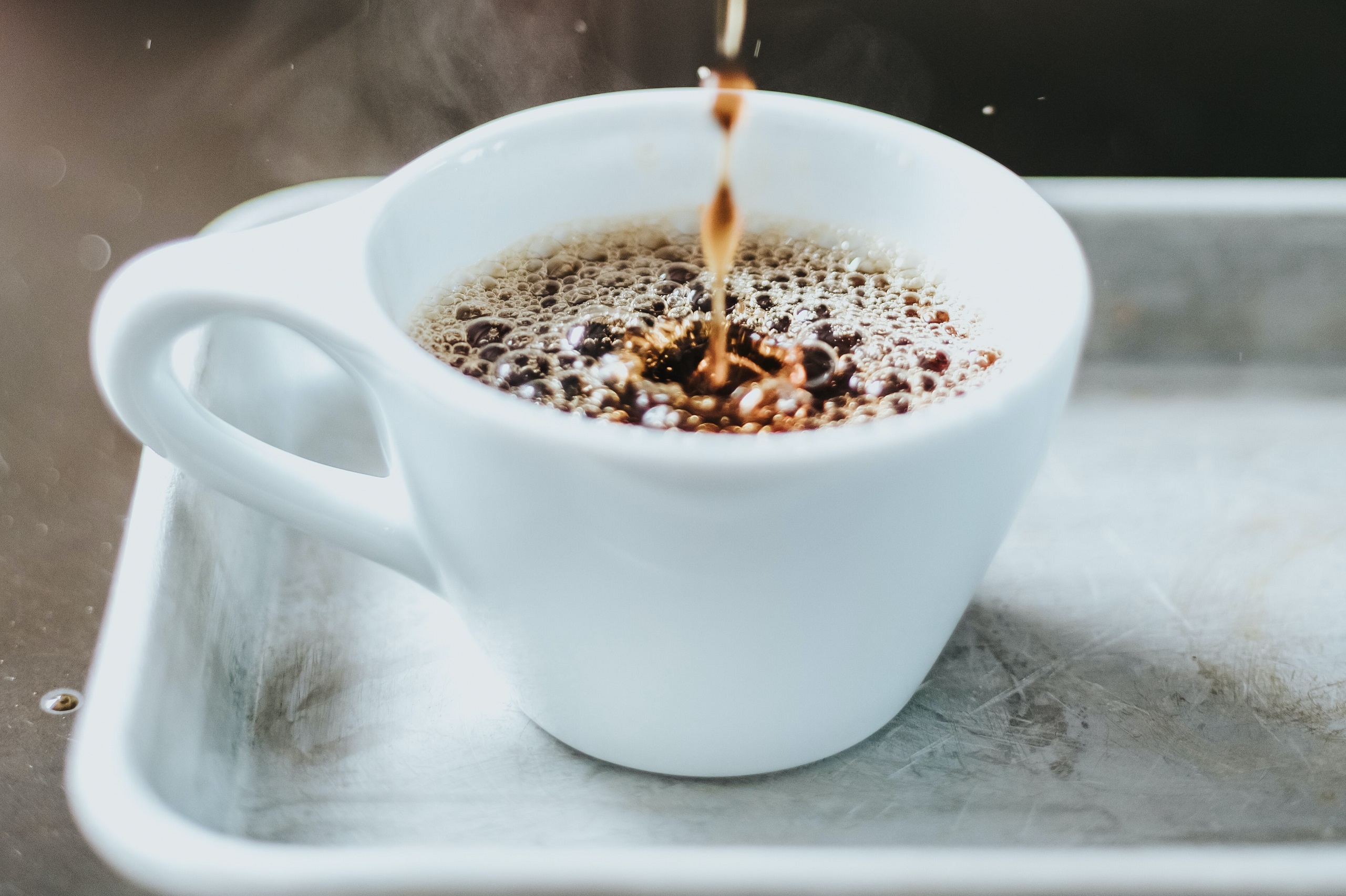 Black coffee drips into a nearly-full white coffee mug