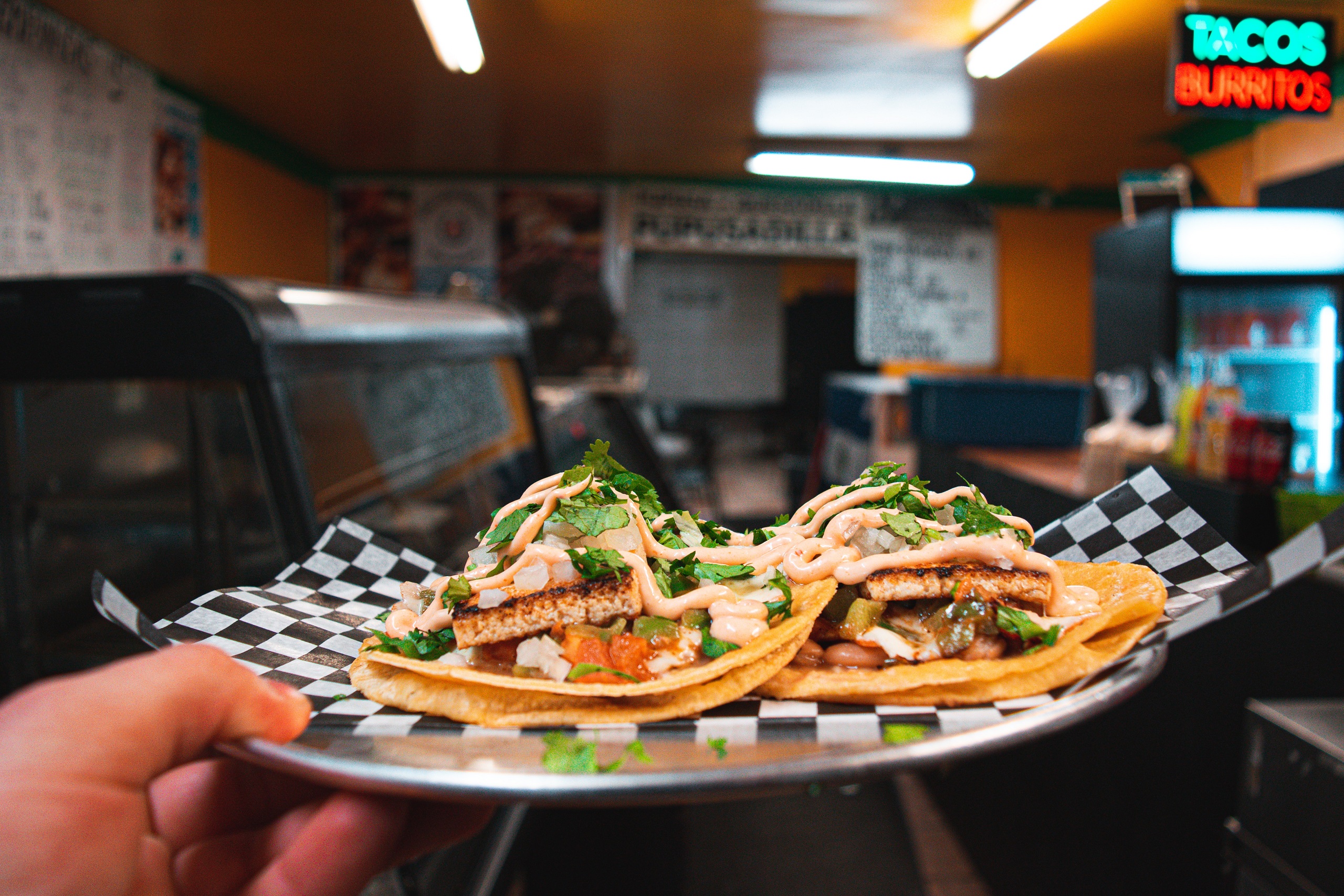 Someone holds up a plate of tacos in a small Mexican restaurant