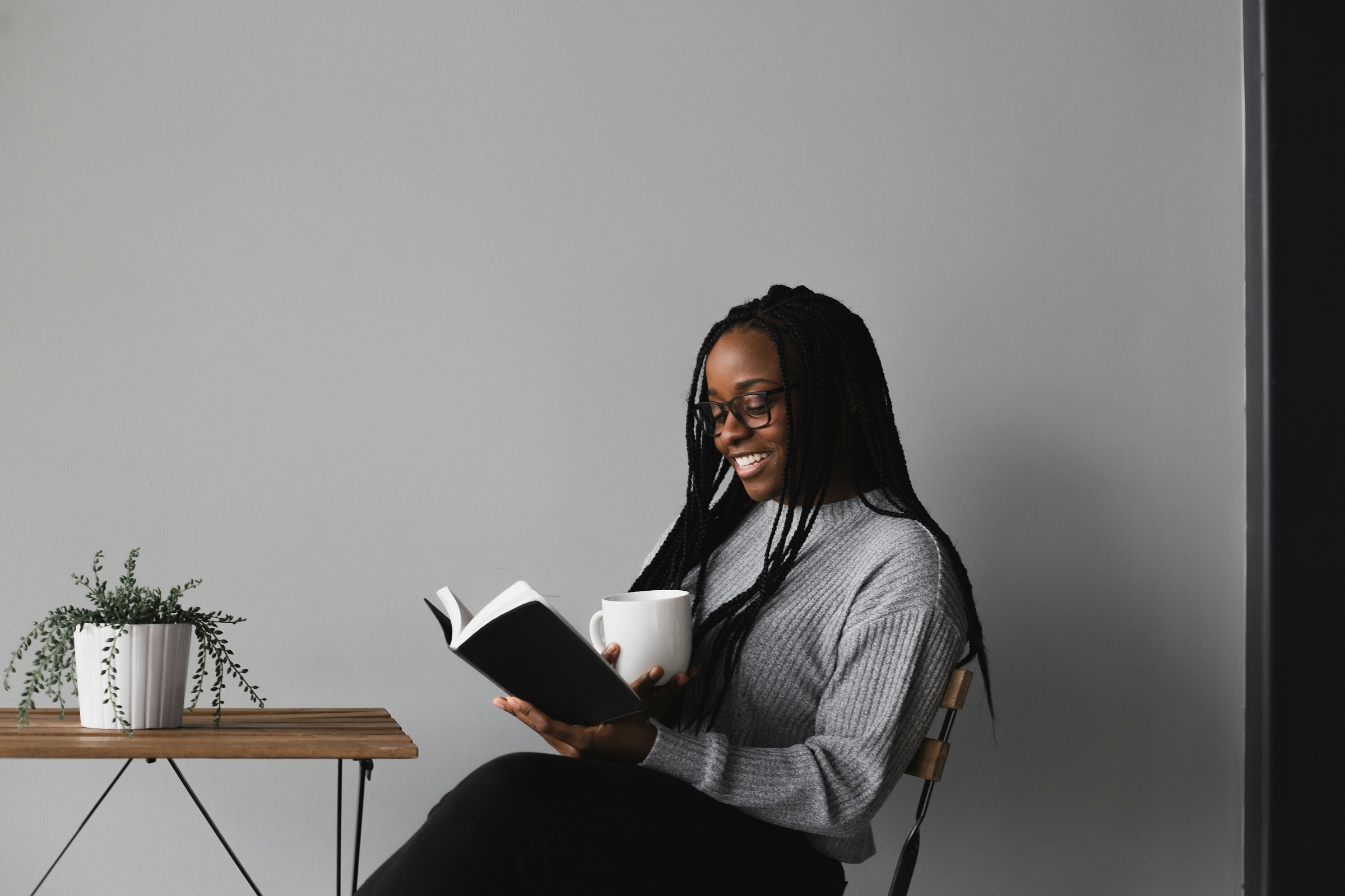 A woman reads as she sits at a table and holds a mug.