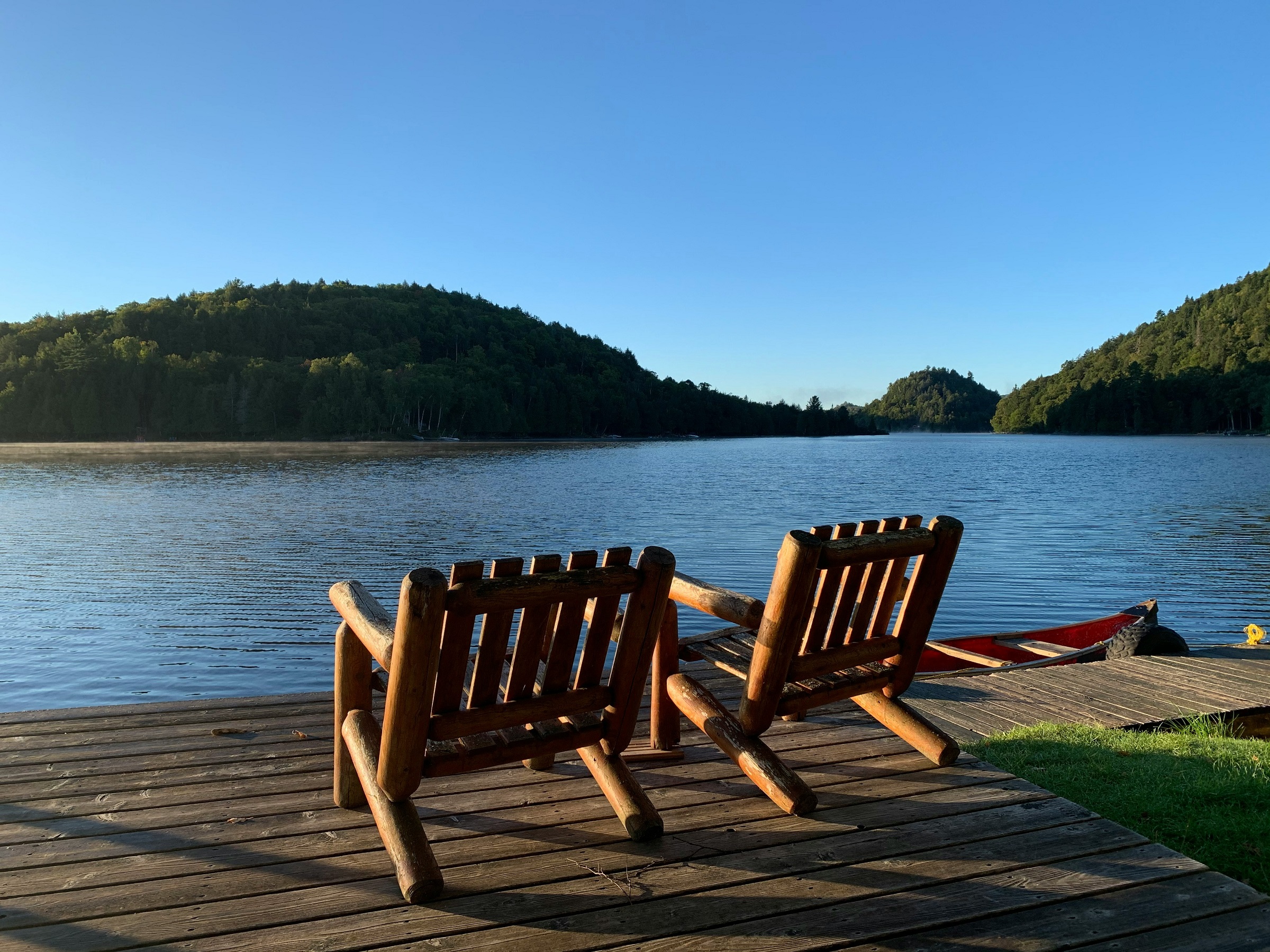 Two wooden chairs sit on a wooden pier looking out over a lake.