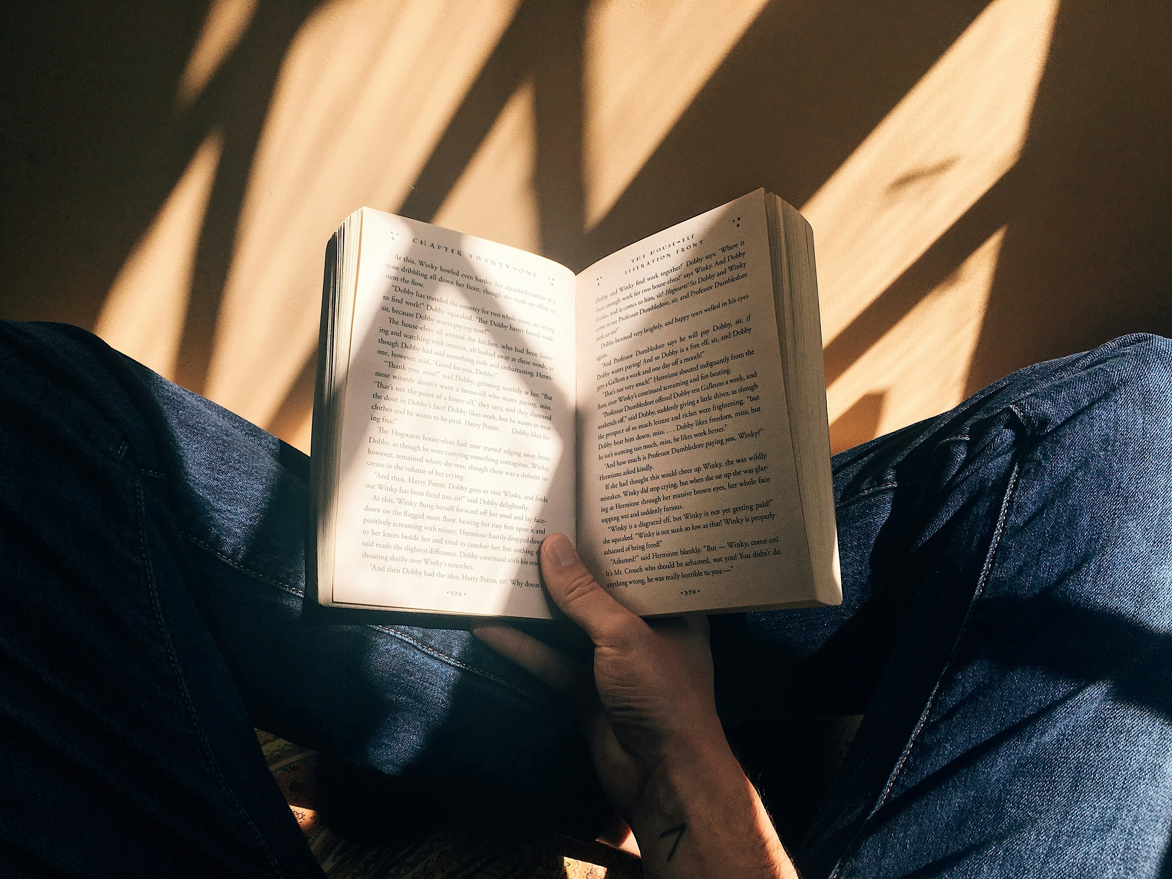 A person holds an open book over their criss-crossed legs.