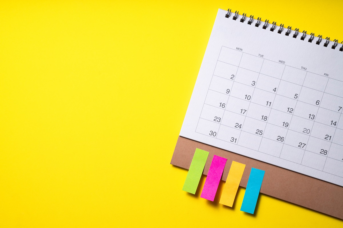 A calendar with four different colored sticky tabs overtop a bright yellow background.