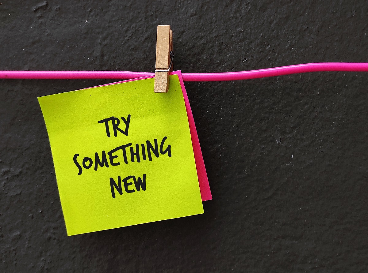 A neon yellow sticky note clipped to a pink string. The sticky note says "Try Something New"