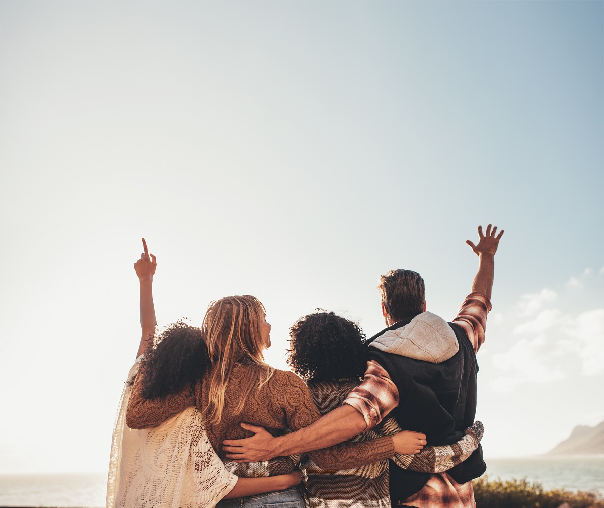 Four friends standing together with their arms raised