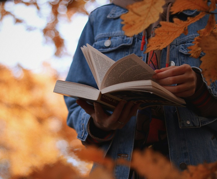 A person holding an open book outside amid some fall leaves