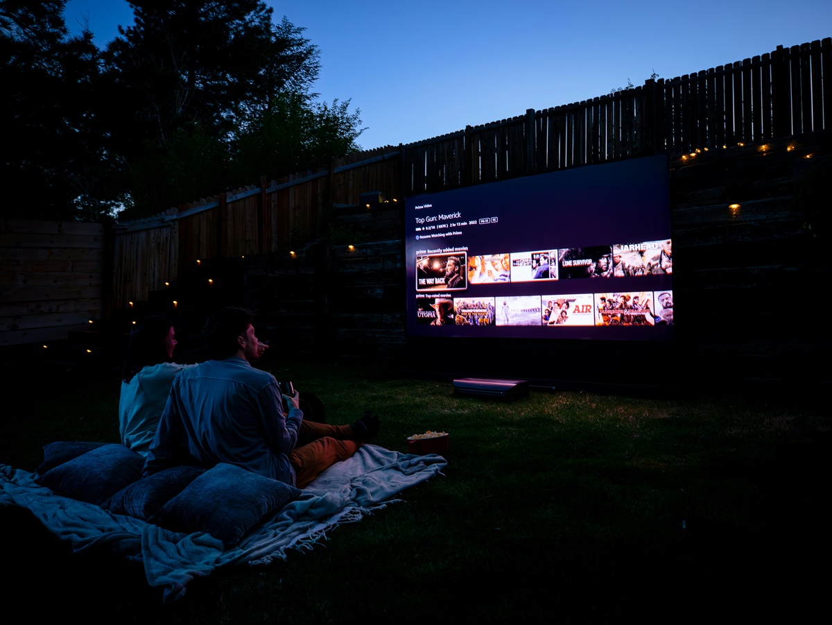 Two people sit on a blanket in the backyard in front of a projector screen as they pick a movie to watch on Netflix.