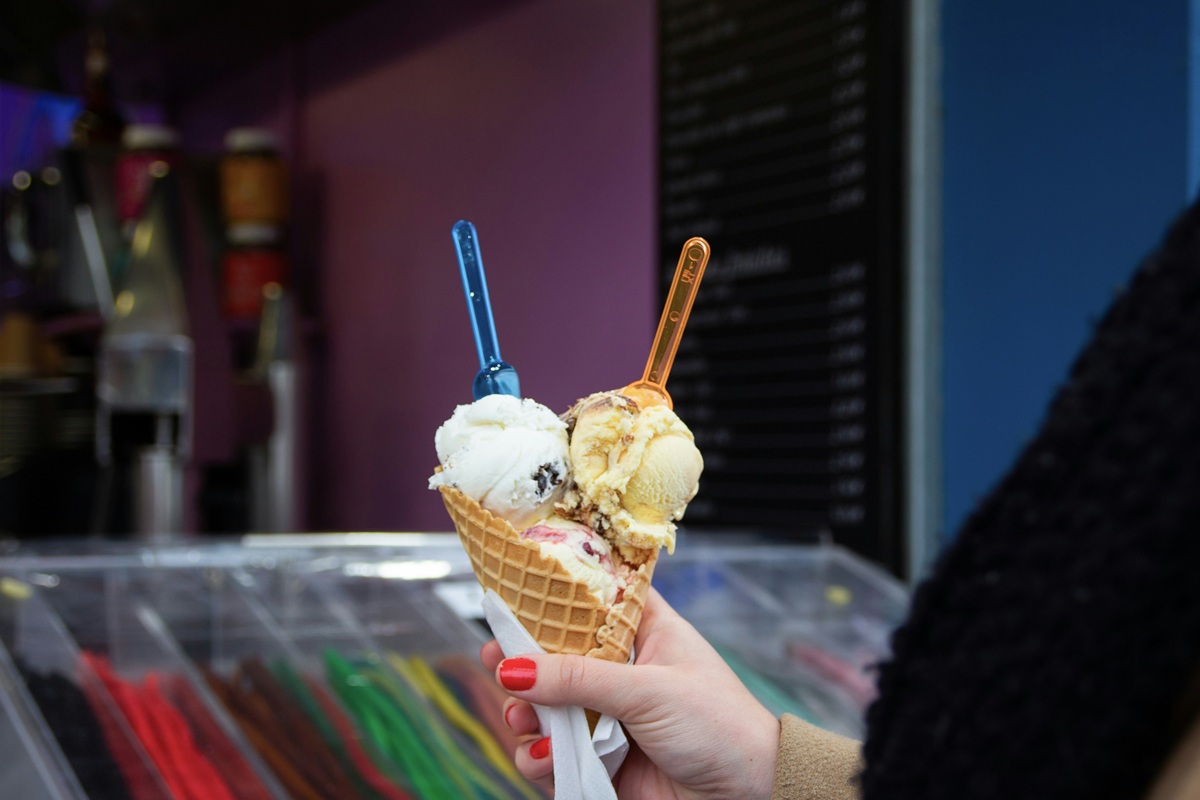 A person holding a waffle cone with three scoops of ice cream