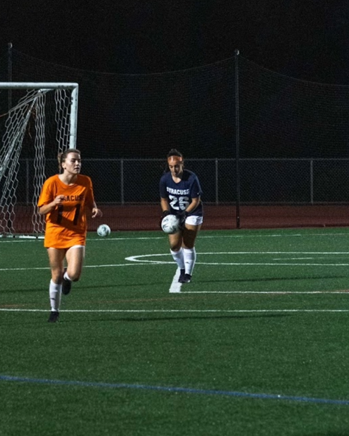 Zoe Rubin plays soccer with another student on a University field.