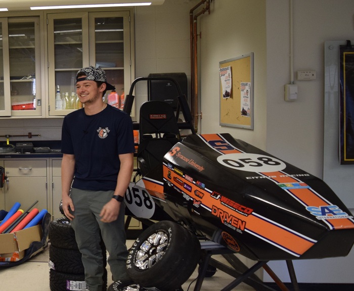 A Syracuse University student stands in front of their Recognized Student Organization club racing car during an interview.