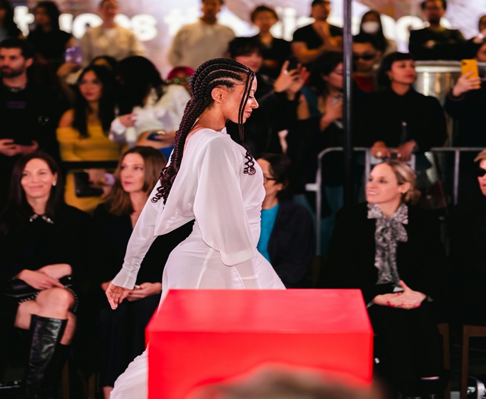 A fashion model walks on a runway in front of audience members.