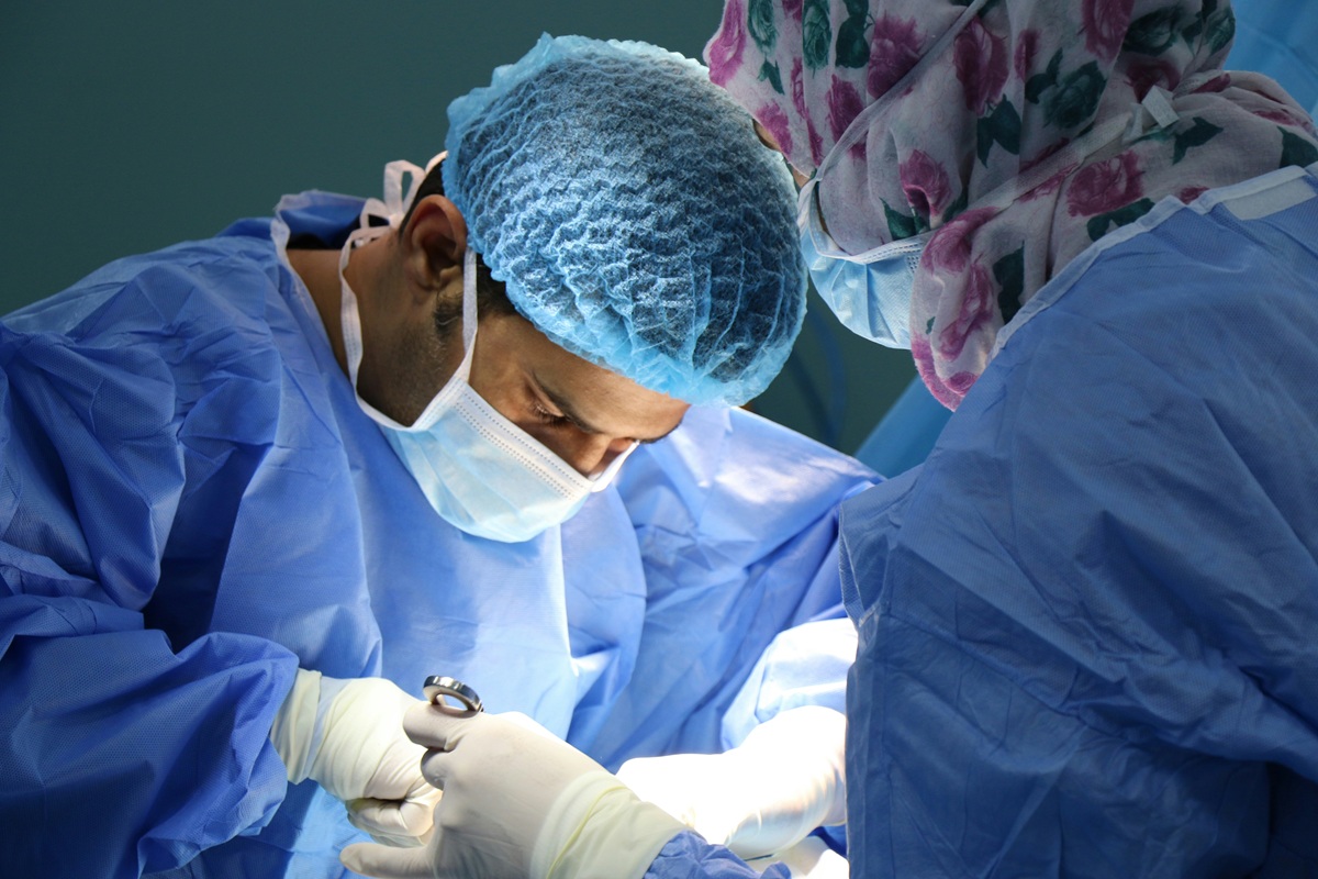 Two doctors in scrubs, masks and hairnets perform a medical operation out of frame of the photo.