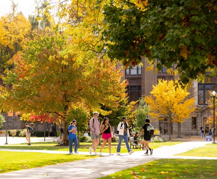 Students walking on campus in the fall. The leaves are bright orange and yellow.