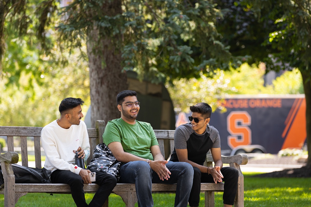 Three men sitting on a bench with an SU truck.