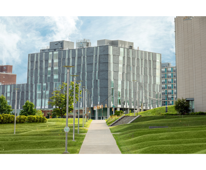 Exterior view of Ernie Davis Hall at Syracuse University, a modern gray brick residence hall surrounded by green lawns, trees and campus walkways.