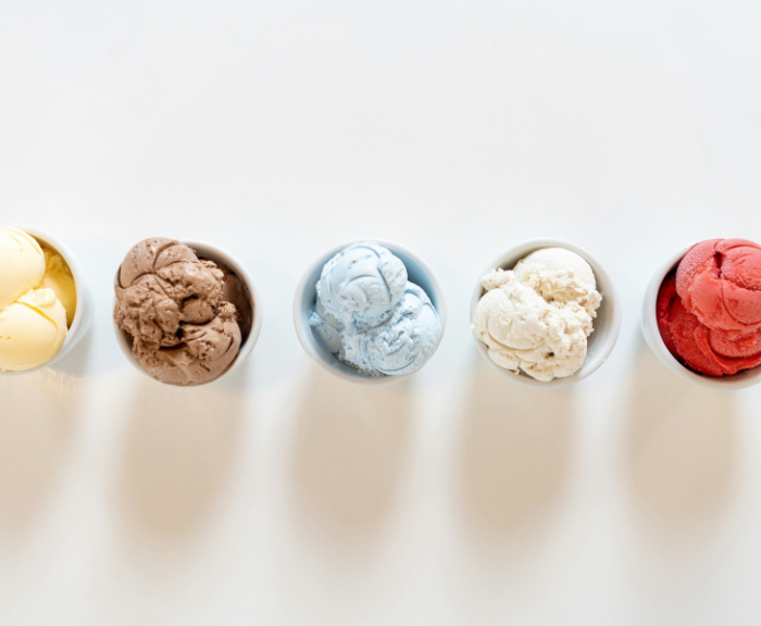 Five small bowls of ice cream in different colors and flavors arranged in a row on a white surface.