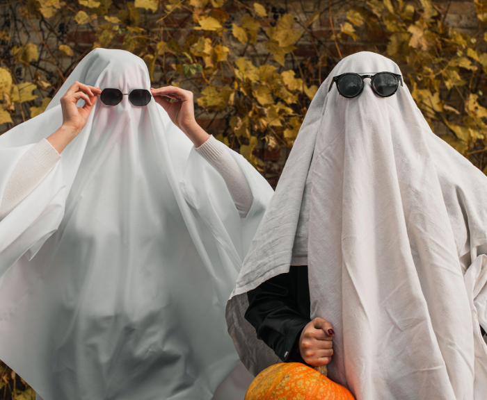 Two people dressed as ghosts with sunglasses surrounded by leaves