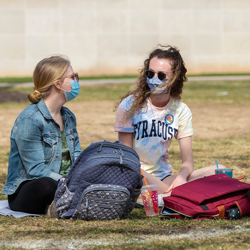 Two students talking while sitting on a blanket on grass