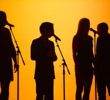 Silouette of four singers on a stage with microphones