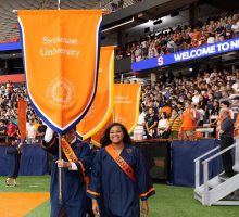 Senior class marshals hold Syracuse University flag while processing in gowns