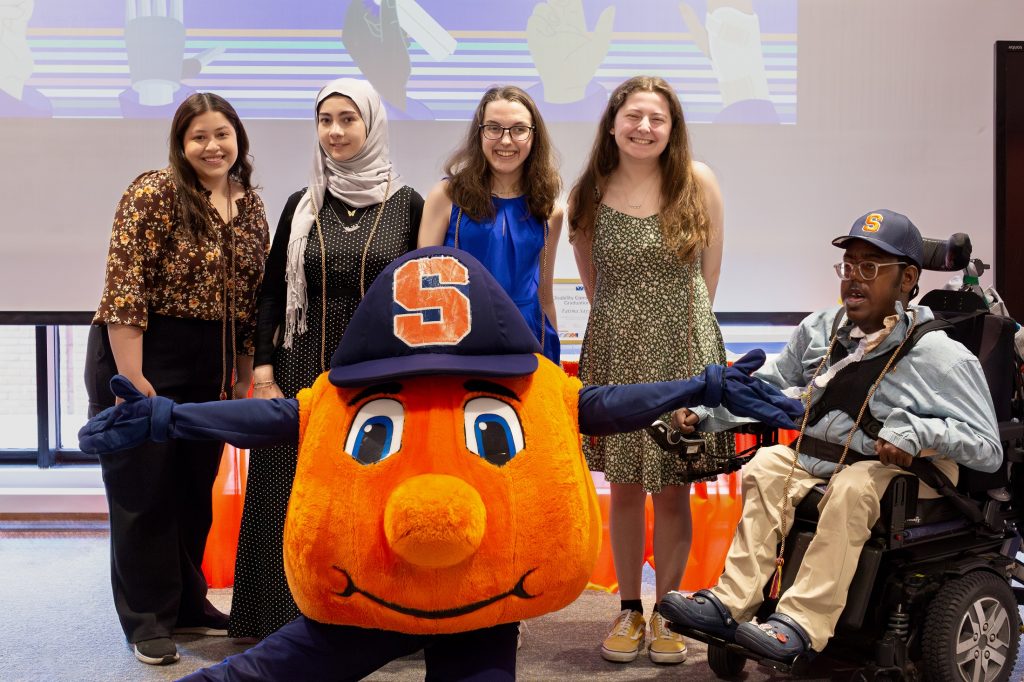 Students honored at the 2024 Disability Community Graduation take a photo together with Otto the Orange.